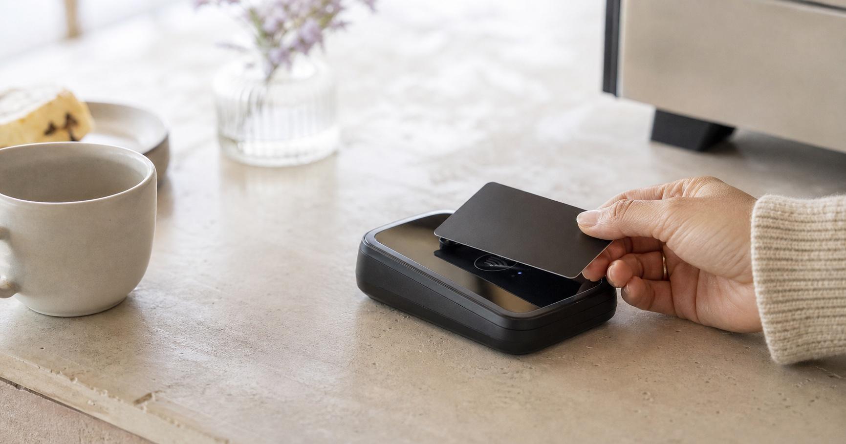 A hand tapping a plain graphite payment card at a café